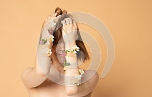 Pretty young girl covering face with hands with flowers and plasters, concept photo for feminist or beauty blog