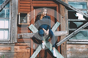 A pretty young girl in good mood is sitting at the doors of an old house. Hipster style, soft colours, vintage