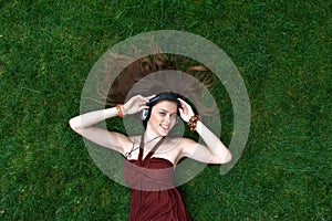 Pretty young girl listen music in headphones lying on grass