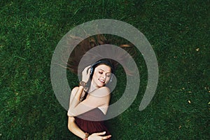 Pretty young girl listening music in headphones lying on grass