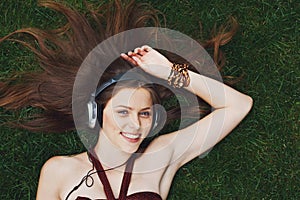 Pretty young girl listening music in headphones lying on grass