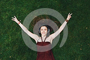 Pretty young girl listening music in headphones lying on grass