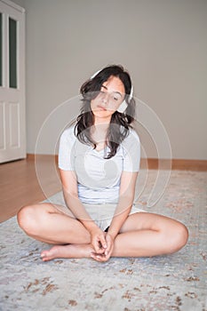 Pretty young girl listening to music with headphones while sitting on carpet at home. Apartment living. Home life