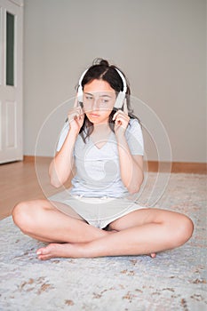 Pretty young girl listening to music with headphones while sitting on carpet at home. Apartment living. Home life