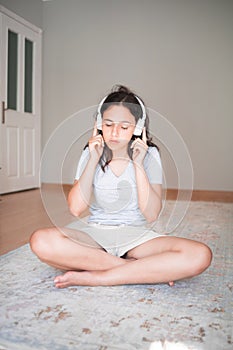 Pretty young girl listening to music with headphones while sitting on carpet at home. Apartment living. Home life