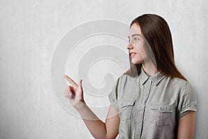 A pretty young girl with long dark hair, nice eyes and charming smile standing sideways on grey background wearing grey T-shirt po