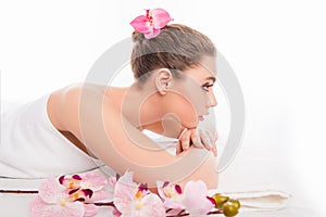 Pretty young girl lying in spa and relaxing with orchid