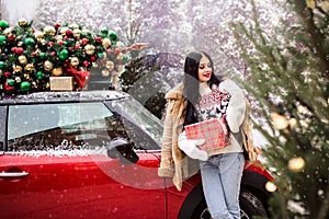 Pretty young girl near red car with decorated xmas tree.