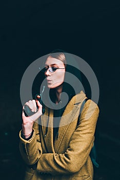 Pretty young girl in olive long coat, hooded sweatshirt. Portrait of woman with hood on dark background