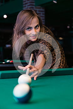 Pretty young girl is playing billiard or pool
