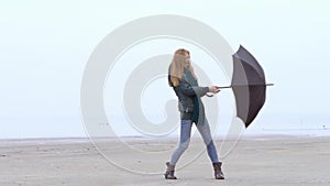 Pretty young girl pulling umbrella against the wind on foggy misty beach