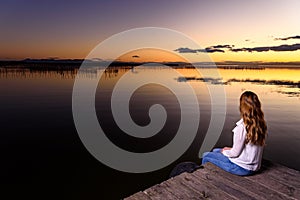 Pretty young girl sitting on the edge of a jetty of a lake at sunset in Valencia