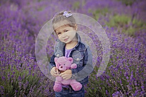 Pretty young girl sitting in lavender field in nice hat boater with purple flower on it.