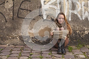 Pretty young girl sitting on the pavement near a stone wall of a house. Walk in the city.