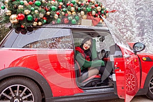 Pretty young girl is sitting in red car with decorated xmas tree on the roof. xmas concept.