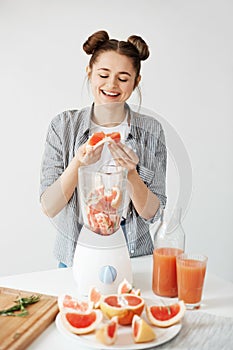 Pretty young girl smiling blending detox refreshing grapefruit smoothie over white wall. Healthy food concept.