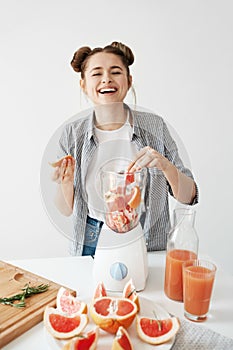 Pretty young girl smiling blending detox refreshing grapefruit smoothie over white wall. Healthy food concept.