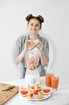 Pretty young girl smiling blending detox refreshing grapefruit smoothie over white wall. Healthy food concept.