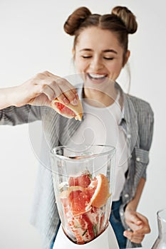 Pretty young girl smiling blending detox refreshing grapefruit smoothie over white wall. Healthy food concept.