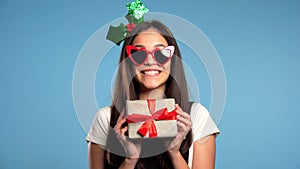 Pretty young girl smiling after received gift box on blue studio background.