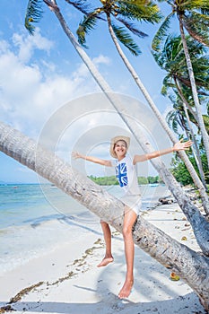 Pretty young girl. Smiling and sitting on palm tree at the tropical island beach with clear water.