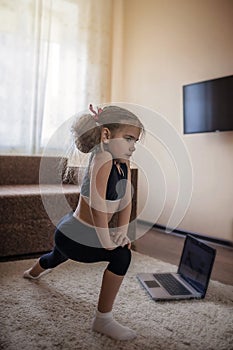 Pretty young girl in sportswear watching online video on laptop and doing fitness exercises at home