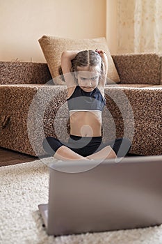 Pretty young girl in sportswear watching online video on laptop and doing fitness exercises at home