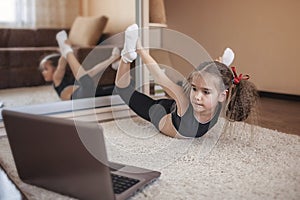 Pretty young girl in sportswear watching online video on laptop and doing fitness exercises at home