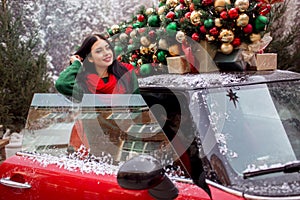 Pretty young girl is standing near red car with decorated xmas tree on the roof, holiday concept.