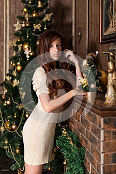 Pretty young girl stands near a decorated fireplace and a Christmas tree