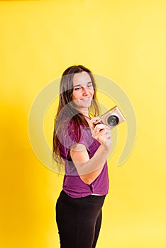 Pretty young girl takes photos with an evil camera, isolated on yellow studio background
