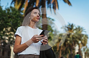 Pretty young girl walks through the Park after office work and chats in messengers with colleagues manager using Internet device