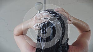 Pretty young girl washes away the shampoo from her hair while standing under a warm shower stream. Concept of