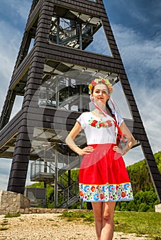 Pretty young girl in white shirt and red skirt posing in front of lookout tower called Heart of Terchova in Slovakia