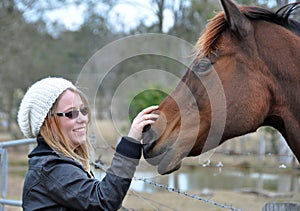 Pretty young happy woman outdoors with pet horse stroking him