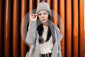 Pretty young hipster woman in fashionable clothes straightens glasses. Fashion portrait beautiful girl model in beige sweater in