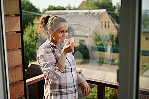 Pretty young Hispanic woman relaxing on balcony holding a cup of coffee or tea