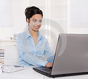 Pretty young indian businesswoman sitting at desk writing a mess