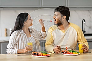 Pretty young indian woman feeding her husband, kitchen interior