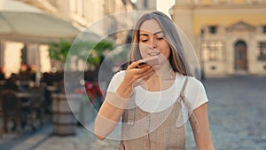 Pretty Young Lady in Casual Wear Speaking in Microphone on Modern Smartphone While Walking Outdoors. Caucasian Girl