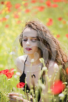 Pretty young lady sitting among poppies field