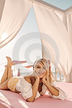 Pretty young lady is sunbathing lying in front on beach bed with canopy near sea.