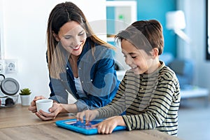 Pretty young mother drinking coffee while her son play with the digital tablet at home