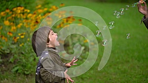 Pretty young mother with her a very cute young son happily blow bubbles outdoors in summer. slow-motion