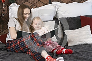 Pretty young mother reading book to her daughter in bed on Christmas eve. Mom or baby sitter telling fairy tale to preschool kid