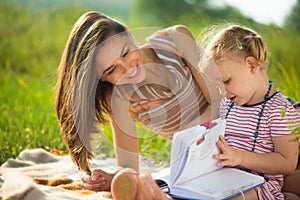 Pretty young mother reading book to her little daughter