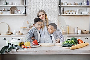 Pretty young mother and two children sons preparing salad with fresh vegetables