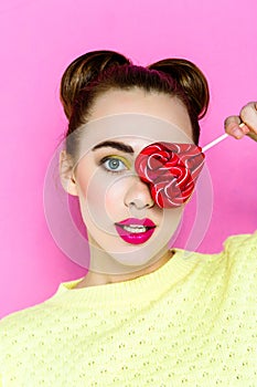 Pretty young playful girl holding heart-shaped lollipop