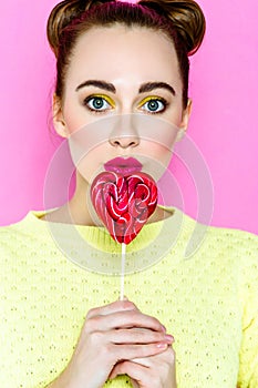 Pretty young playful girl holding heart-shaped lollipop