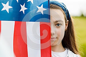 Pretty young pre-teen girl in field holding American flag.